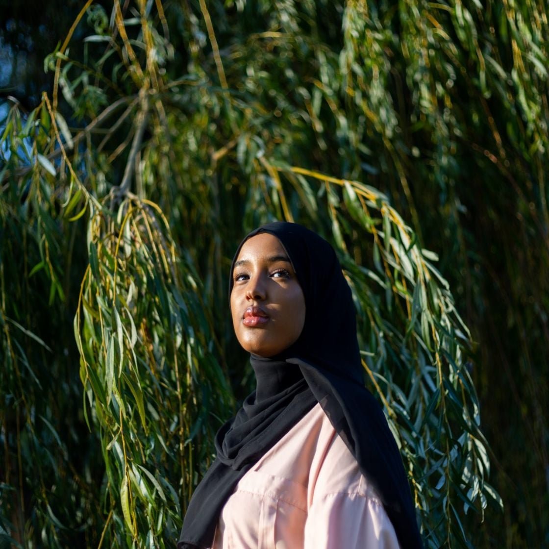 A woman wearing a hijab stood in front of a tree