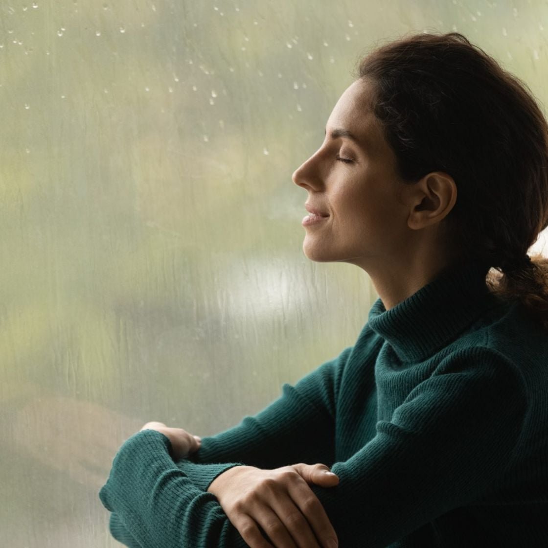 A woman breathing deep at home in front of a window