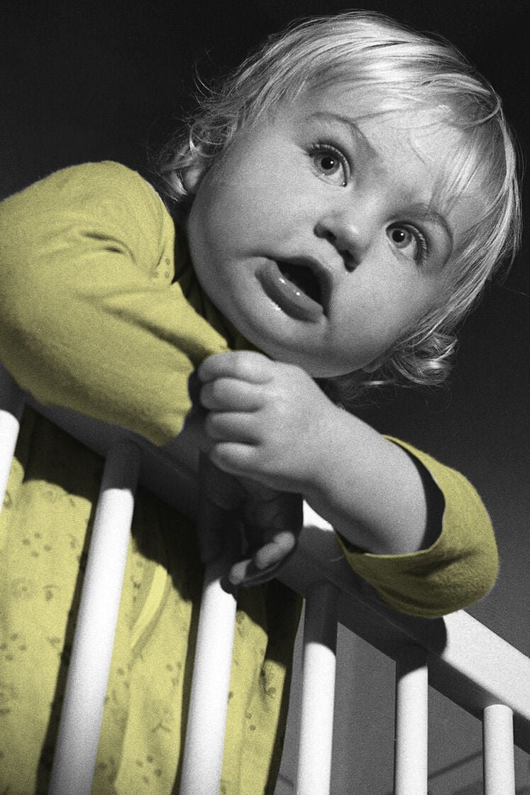 A baby hanging over a cot