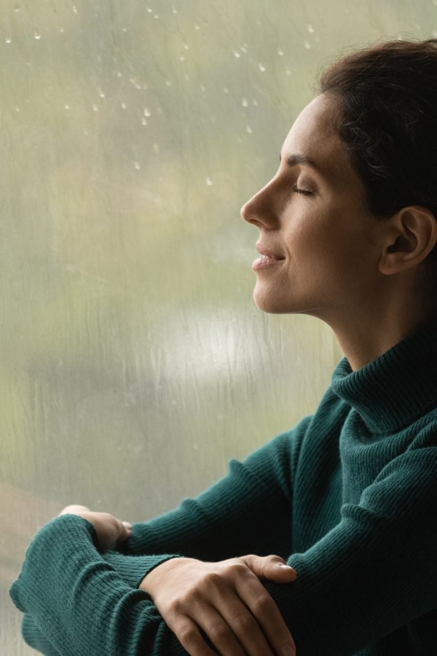 A woman breathing deep at home in front of a window