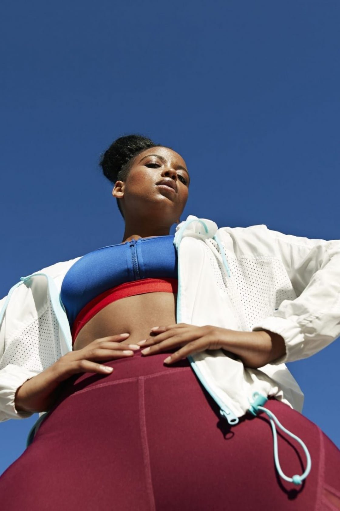 A woman wearing purple leggings, a blue sports bra and white jacket stood outside.