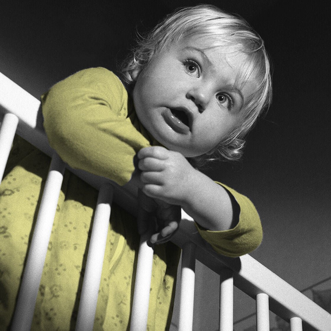 A baby hanging over a cot