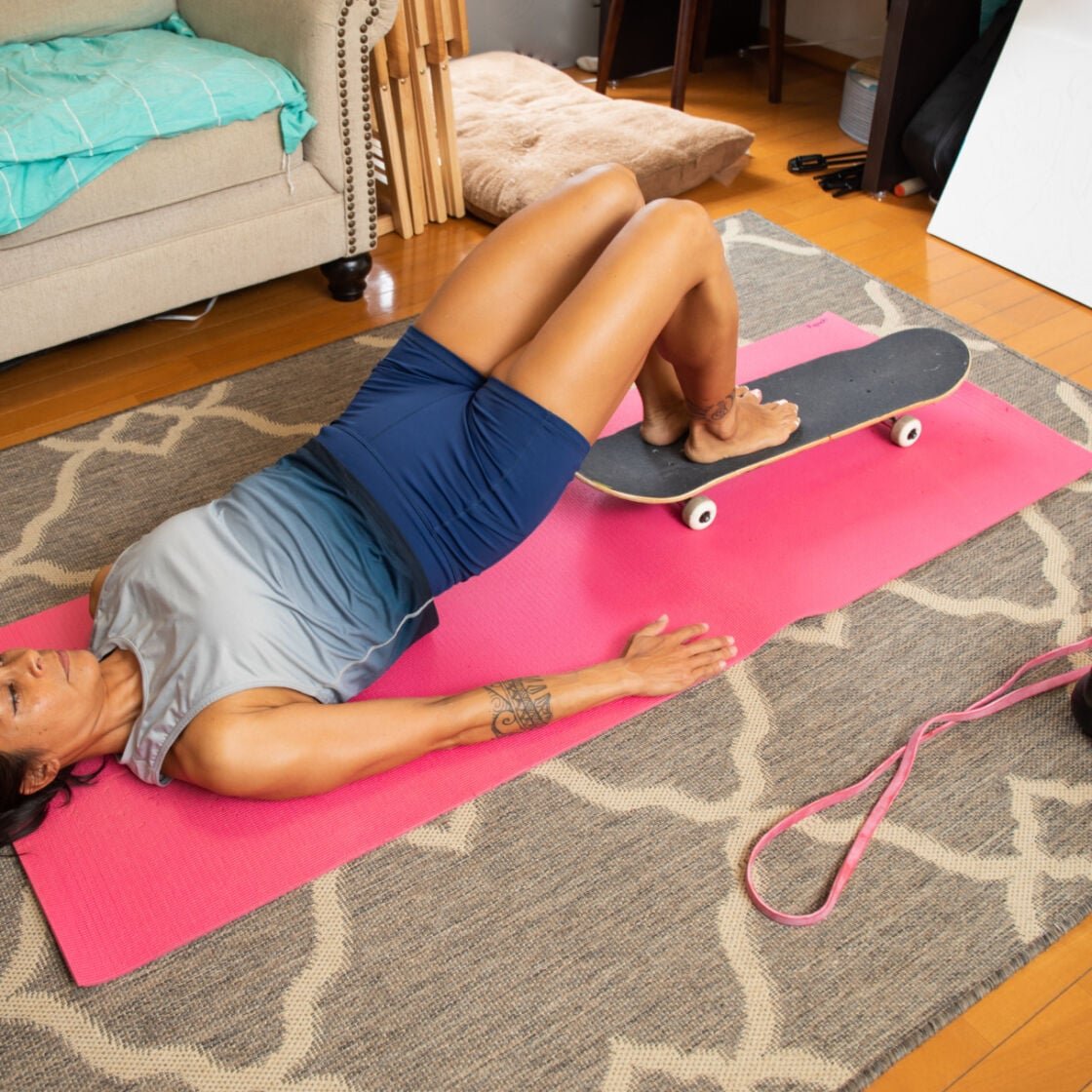 A woman doing an at-home workout using a skateboard to mimic reformer pilates